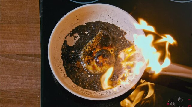 fire burns in a pan. burnt egg on a white pan on a black stove. fried eggs in black oil, similar to unfiltered petroleum products. boiling dark oil frame from above 100fps 2.8k top shot