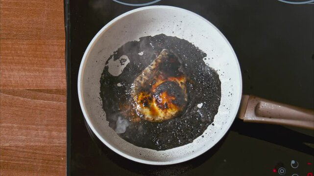 burnt egg on a white pan on a black stove. fried eggs in black oil, similar to unfiltered petroleum products. boiling dark oil frame from above 100fps 2.8k