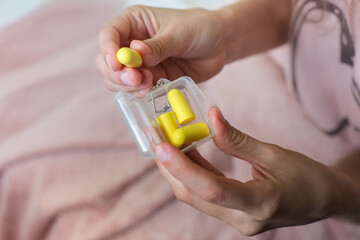 Close up of female hands and yellow earplugs. Woman holding a box of earplugs. Light background.