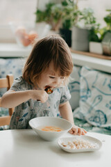 a little girl is sitting at the kitchen table eating soup