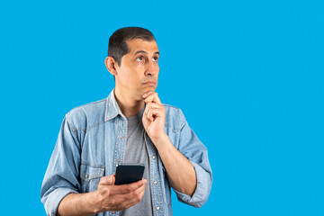 Studio shot of a handsome man using smartphone standing over isolated blue background serious face...