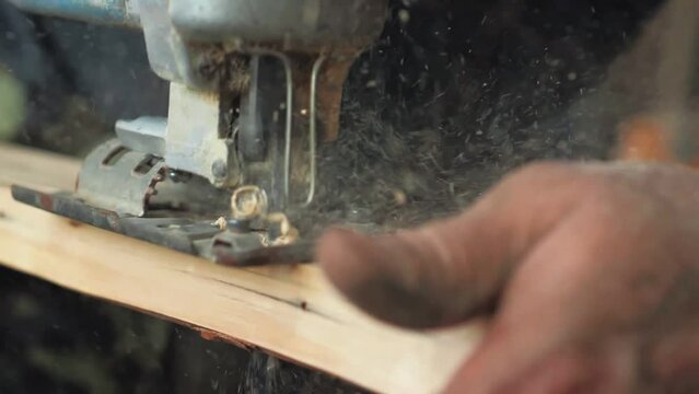 Close-up, a carpenter in his workshop saws an electric jigsaw, a wooden board, makes furniture parts. Woodwork.Slow-motion Carpenter saws wood, processing it. Home Repair Construction Tools