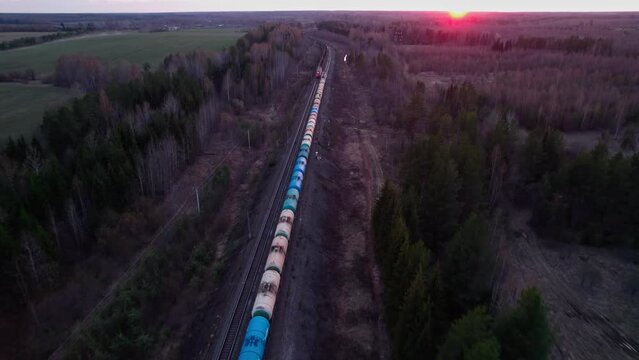Two long trains ride under the rays of the sunset.