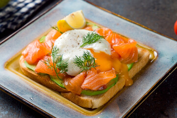 poached egg with salmon and avocado on bread, bruschetta, sandwich on dark stone table macro close up