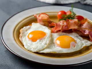 Fried eggs with tomatoes and bacon on blue concrete table macro close up