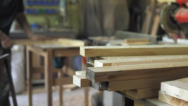 In the background, out of focus, a carpenter is in the workshop, working with wood, making furniture parts in natural light. A woodworking milling cutter removes chamfers from the edge.Carpentry tools