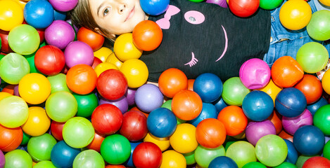 Fototapeta na wymiar Kind liegt in einem Ballpool, bunte Bälle und ein Mädchen