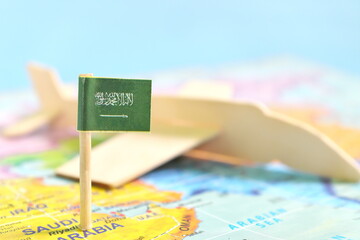 Selective focus of Saudi Arabia flag in blurry world map and airplane model. Travel and tourism destination concept.