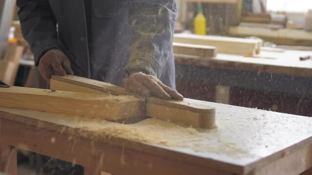 A woodworking milling cutter removes chamfers from the edge of a board with a large amount of sawdust.Carpenter in the workshop, works with wood, makes furniture parts in natural light.Carpentry tools
