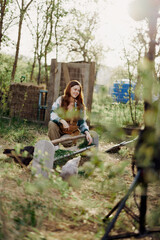 Naklejka na ściany i meble A woman pours food into a bird feeder while sitting in a chicken pen in the countryside on a summer day in the sunlight. The concept of ecological care and organic farming