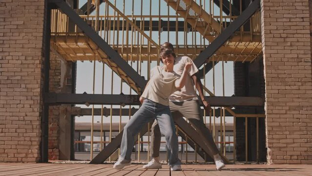 Stab slowmo of diverse millennial couple of bloggers having fun while dancing outdoors at construction site on warm sunny day