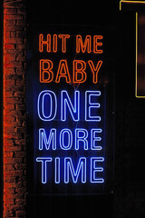 Blue and Red neon light lettering "Hit me baby one more time" in dark, restaurant or cafe. Front view, closeup, vertical photo.