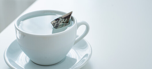 Dollar origami boat in a cup of water on a white table. The concept of financial success, the...