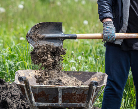A man is digging soil into a cart with a shovel.