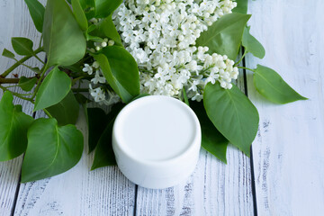 One white box with cosmetic products and creams with fresh, blooming and fragrant lilac flowers and free space for advertising.