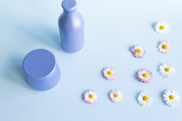 Fresh flowers, daisies are laid out in a corner and two purple jars with cream cosmetics on a blue background and a free space for advertising.