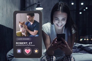 Smiling woman in pajama sitting on bed liking profile of man in dating app on phone - obrazy, fototapety, plakaty