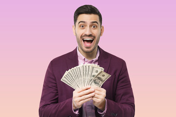 Successful excited man in suit holding bunch of money cash isolated over pink background