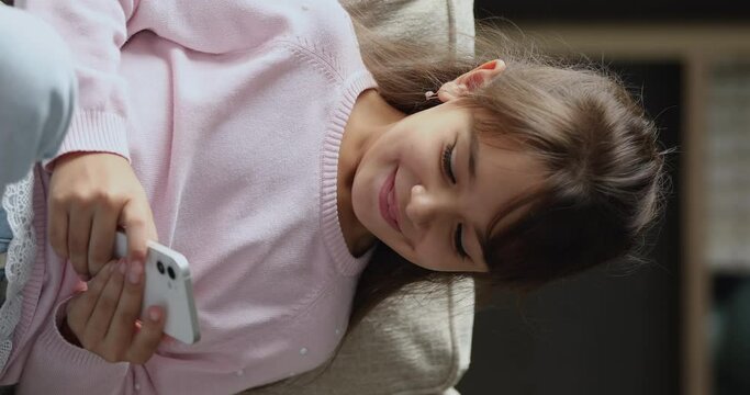 Close up vertical view little laughing girl play games on cellphone, spend time on internet. Young gen Z use modern wireless tech, parental control software app for kids safety on cyberspace concept