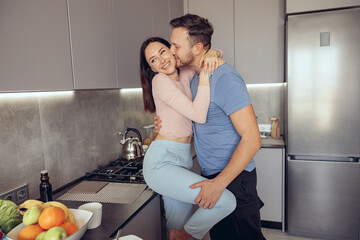 Caucasian handsome man kissing beauiful woman while couple standing in kitchen.