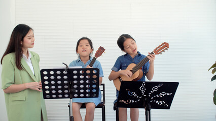 Happy Asian two siblings learning play skill guitar togetherness with teacher woman in...