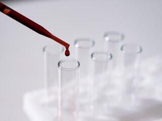 Close-up of a laboratory assistant dripping blood from a pipette into a test tube on a white background. 