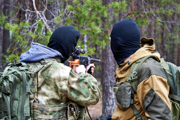 A man in a balaclava with a sniper rifle aiming in the woods