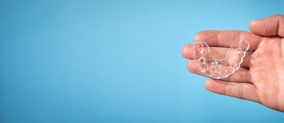  Male hand showing transparent aligner on the blue background.