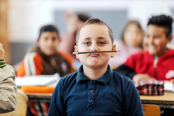 A silly schoolboy making jokes and pretending a pencil is a mustache. - obrazy, fototapety, plakaty