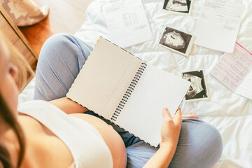 Baby list pregnant woman. Young pregnancy mother holding notepad. Pregnant lady writing check list of baby. Concept of maternity, expectation.