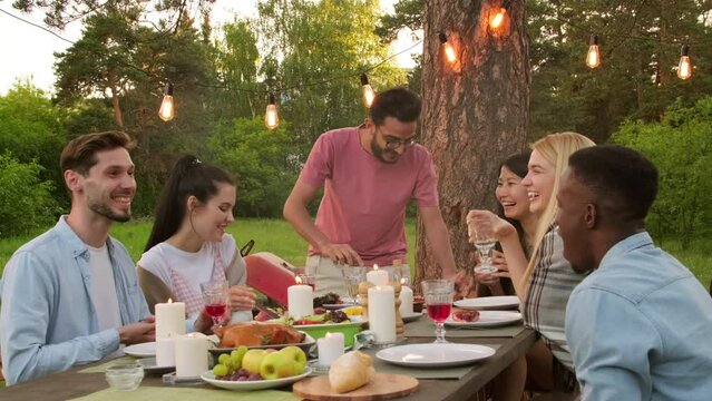 Group of modern multi-ethnic young men and women having fun together in park enjoying dinner celebrating something