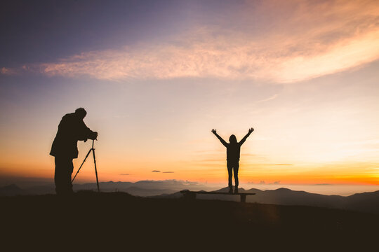 Silhouette of photographer taking photo with model on mountain at sunset, professional wedding photography