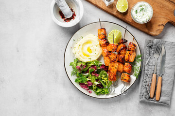 Grilled salmon skewers with fresh salad leaves and mashed potato. Light gray background. Top view