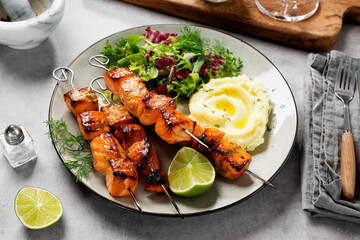 Grilled salmon skewers with fresh salad leaves and mashed potato. Light gray background.