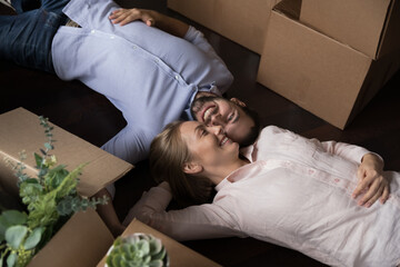Obraz na płótnie Canvas Married homeowner couple lying on floor resting on relocation day near heap of cardboard boxes with packed personal stuff, above view. Mortgage, independence, cohabitation, new home, tenancy concept
