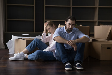 Tired spouses sit on floor near cardboard boxes with stuff, feel exhausted and unmotivated on hard...