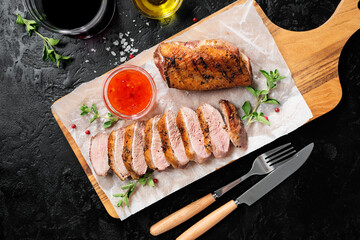 Roasted duck breast served with sauce and fresh herbs. Black background, top view