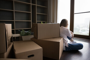 Rear back view young woman sit on floor near heap of cardboard boxes on relocation day. Move-out to...