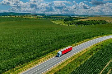 red truck driving on asphalt road along the green fields. seen from the air. Aerial view landscape. drone photography. cargo delivery and transportation concept