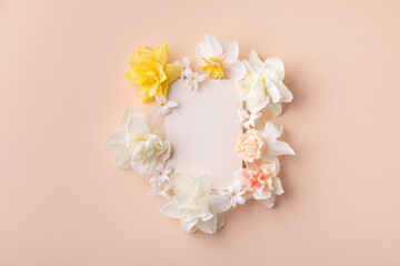 Fototapeta na wymiar Beautiful floral arrangement of white narcissus flowers with paper card for wedding or greeting on peach background. Top view and flat lay.