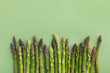 Heap of fresh asparagus on green background top view. Healthy food in flat lay style. - obrazy, fototapety, plakaty