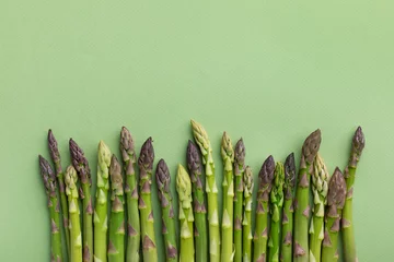 Poster Heap of fresh asparagus on green background top view. Healthy food in flat lay style. © juliasudnitskaya