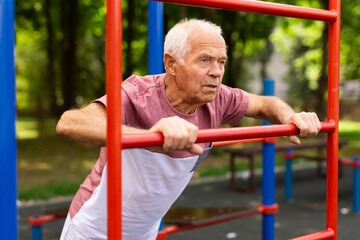 Obraz premium Sportive elderly man doing street fitness on the simulator in park