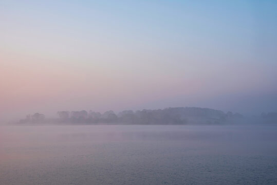 Beautiful landcape image of Spring sunrise over reservoir lake with dawn glow spreading aross the water with low mist adding atmosphere