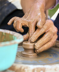 The potter's hands are gently and surely formed by a clay pot on a potter's wheel.