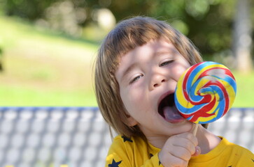 A little boy is enjoying a big candy on a stick. Multicolored lolipop. Summer concept, family holidays, birthday, amusement park, water park