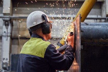 worker repairs a large metal part with an angle grinder