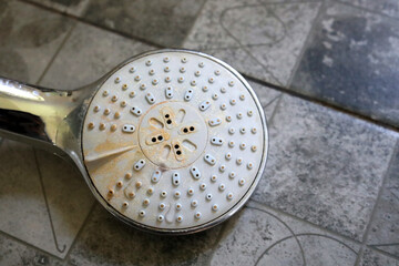 Shower head with limescale close-up. Shower head on tiled floor. Round shower head with clogged...