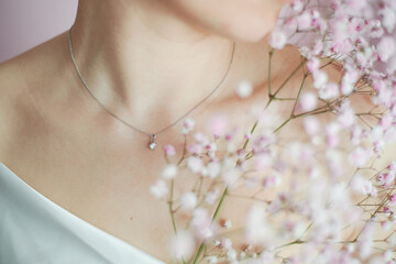 A sprig of pink hippophile, a woman's neck and a silver jewelry with a transparent stone. Tenderness in the advertising of jewelry and perfume. Beauty and women's health. - 508916965