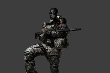 Shot of brave soldier of african ethnic with gas mask holding rifle isolated on dark background.